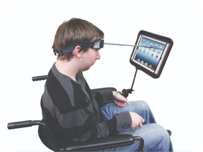 A person taps on
    a tablet mounted to their wheelchair using a wand that extends from their
    forehead.